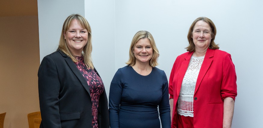 Three caucasian women stand in a row smiling.